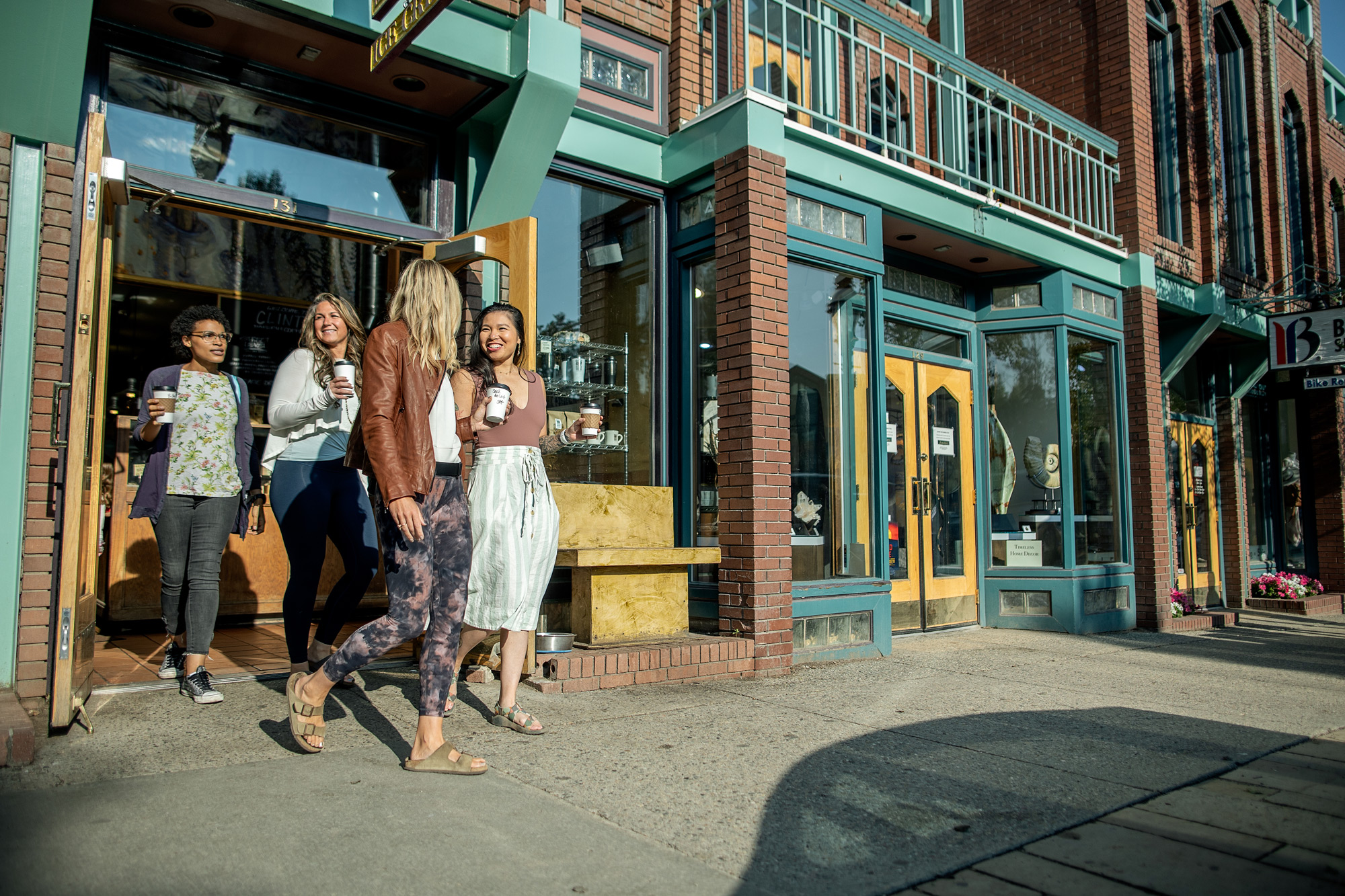 Group of people holding to go cups exiting a shop on a sunny day.